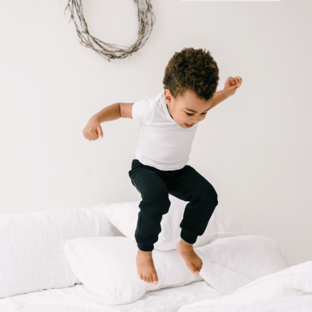 toddler jumping on bed who is overly energetic at bedtime representing signs of overtiredness in toddlers