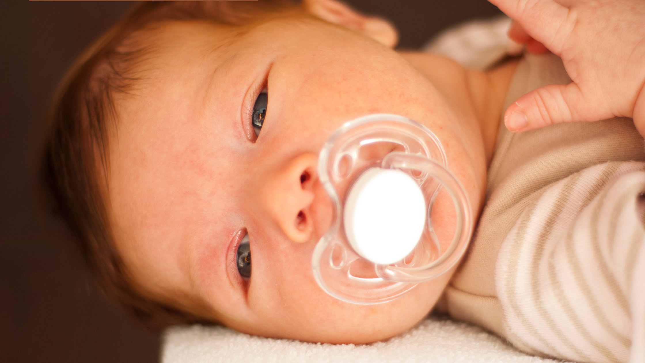 Newborn baby with pacifier lying on blanket, early soothing and sleep support